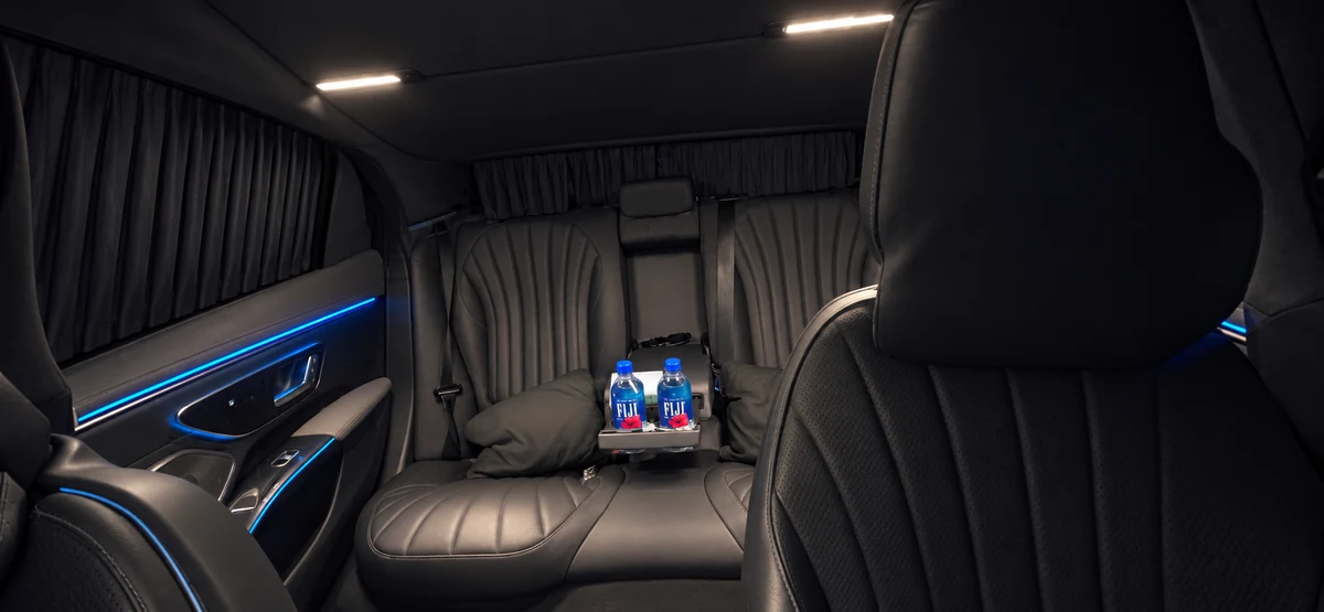 Rear cabin of Arion’s 2023 Mercedes-Benz EQS 450 — black leather seating, blue ambient lighting, privacy curtains and chilled water on the console